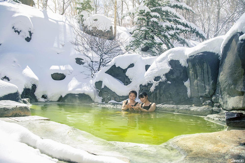 Outdoor winter onsen in Hokkaido surrounded by snow-covered scenery at a traditional Japanese ryokan.